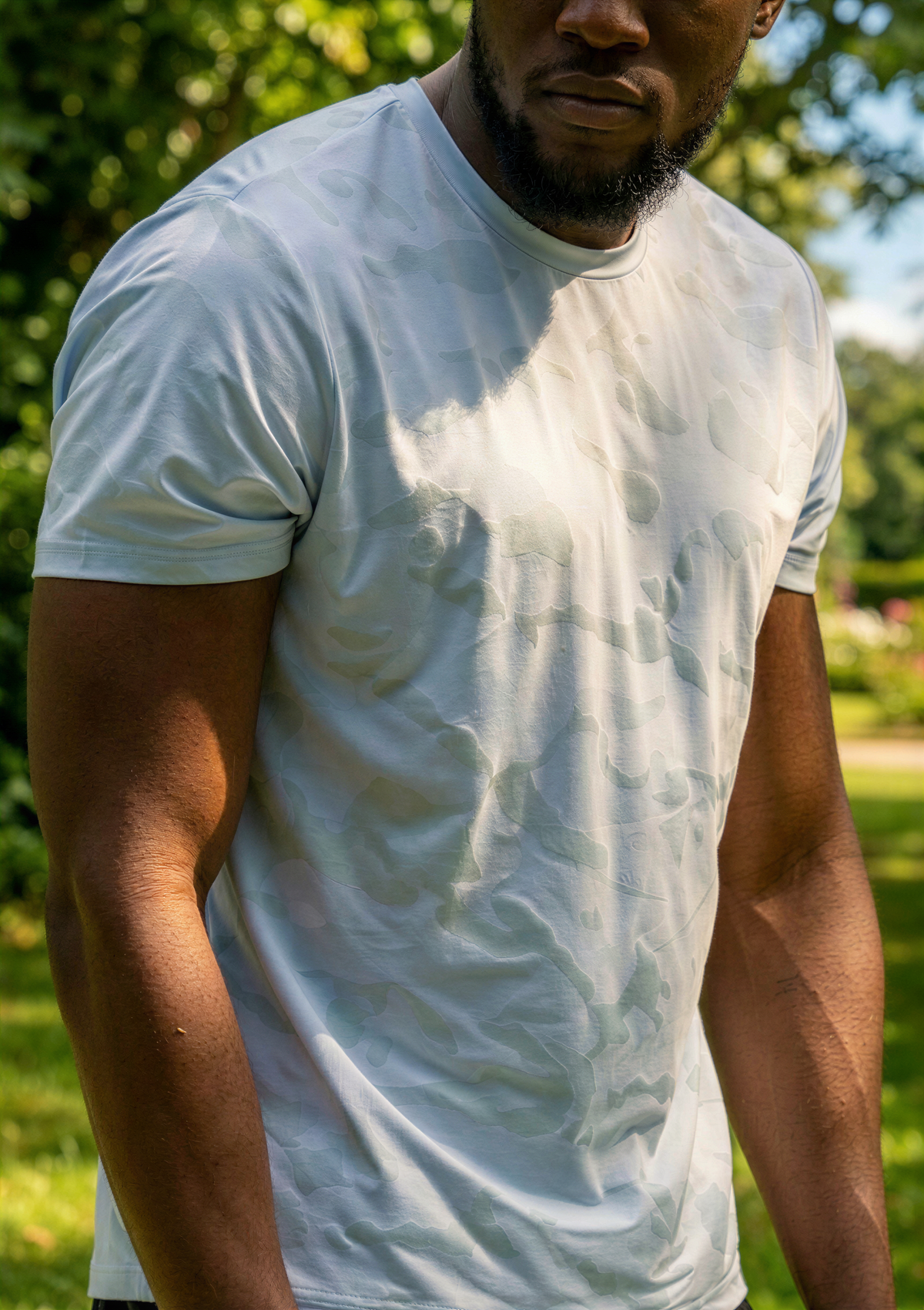A close-up of a man outdoors wearing a white short-sleeve crewneck t-shirt, with sunlight and rain causing heavy waterlogging and wrinkles on the front of the shirt.
