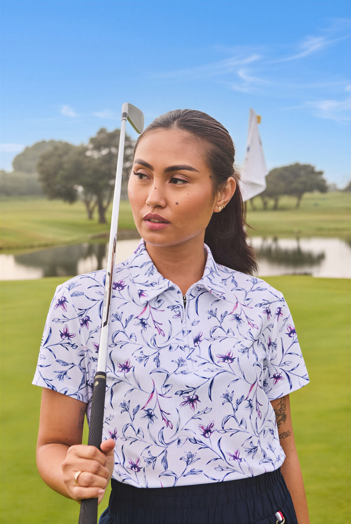 A woman on a golf course wearing a white short-sleeve polo shirt with a blue and purple floral pattern, holding a golf club.
